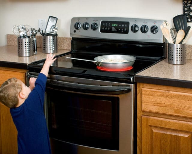 child reaching for hot pan on stove, at risk of burn