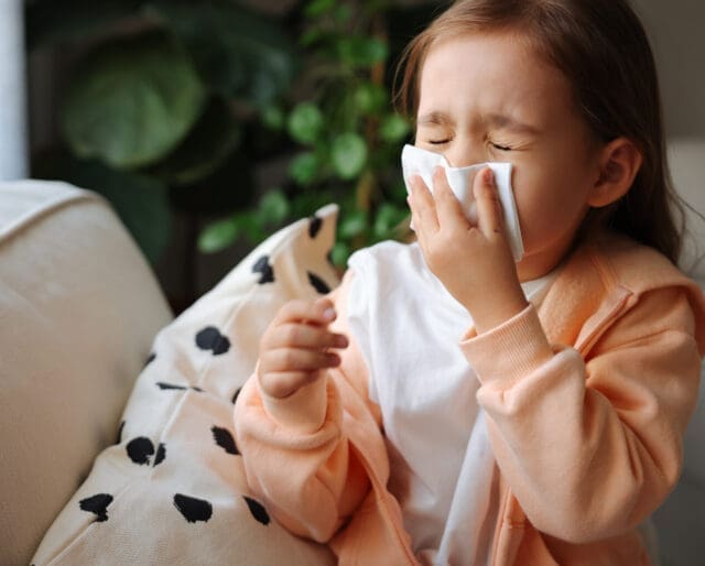 Sick little schoolgirl coughs and blows nose wiping with white paper napkin.