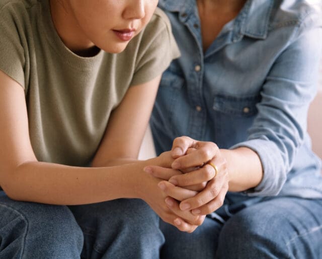 parent sitting and holding teenage child's hands in an embrace in a moment of difficulty