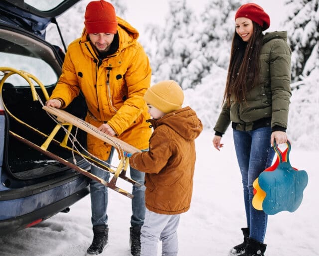 Family loading a sled into the back of a car in snowy weather