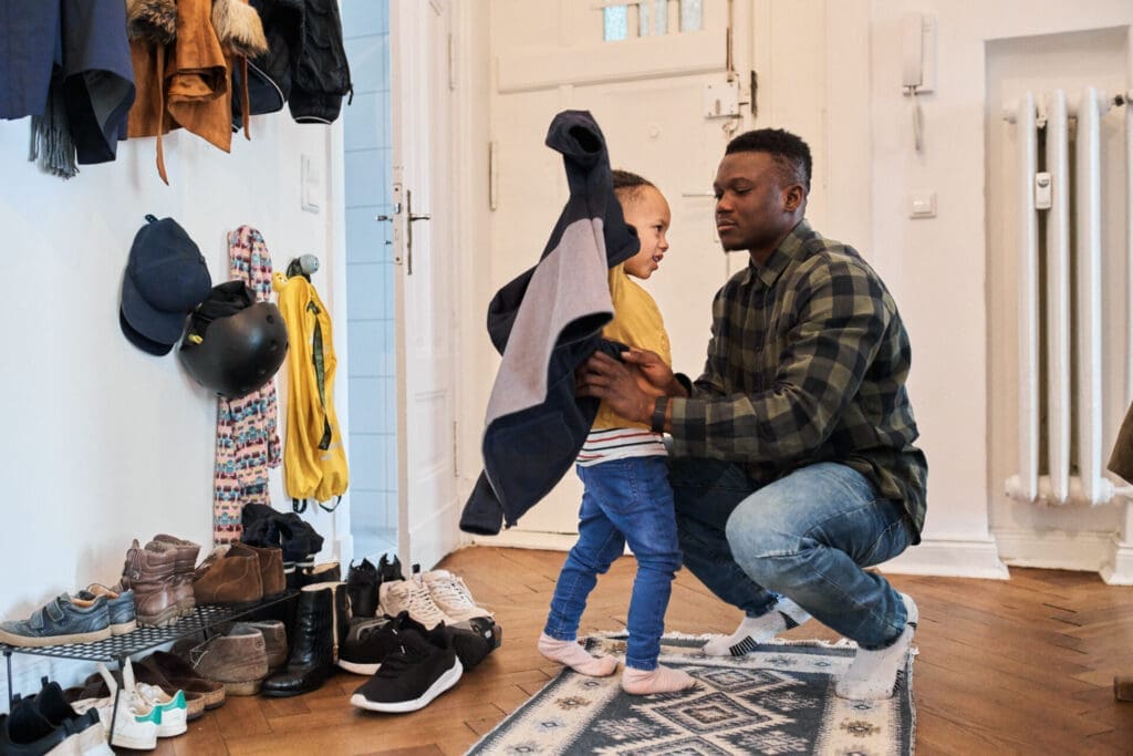 Father helping young son put on a jacket in the middle of a hallway