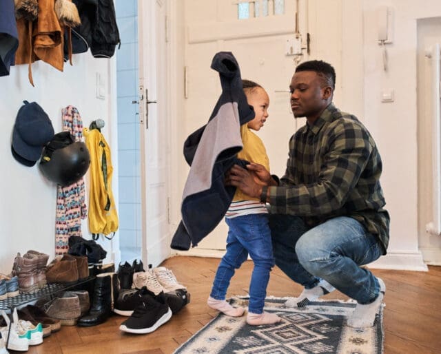 Father helping young son put on a jacket in the middle of a hallway