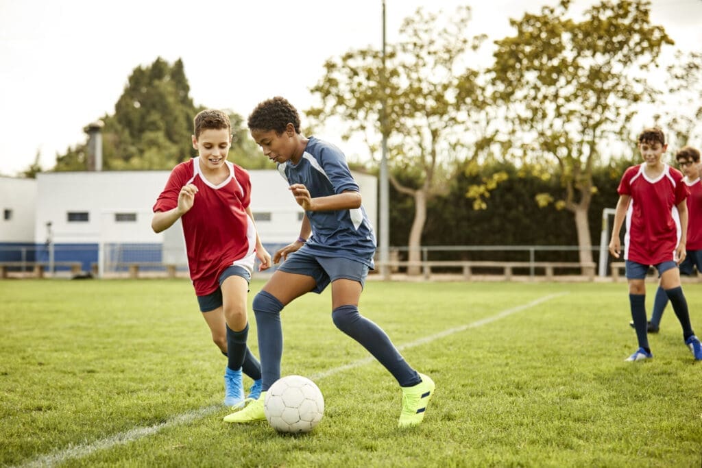 Two boys playing soccer, aiming to kick the ball in between them