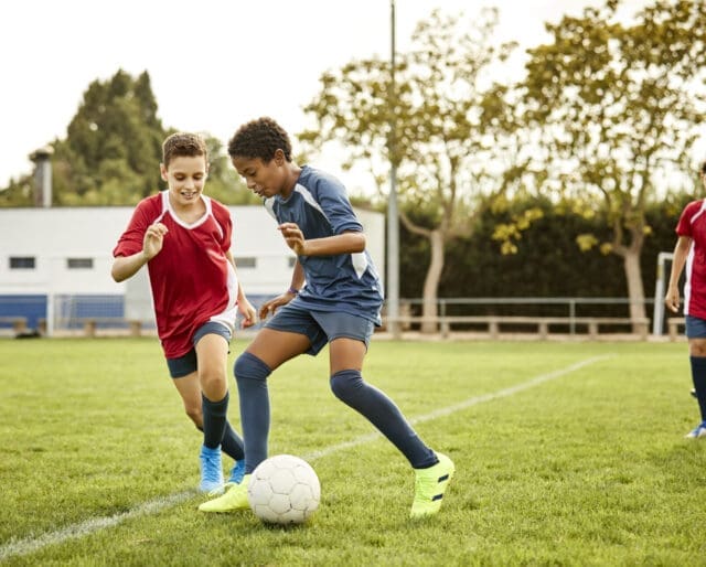 Two boys playing soccer, aiming to kick the ball in between them