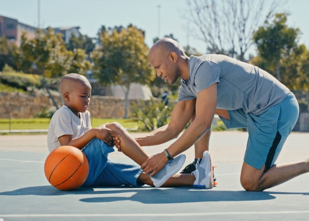father checking on son's knee after he fell down on a basketball court