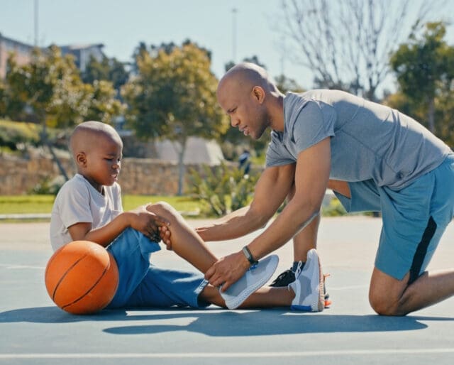 father checking on son's knee after he fell down on a basketball court