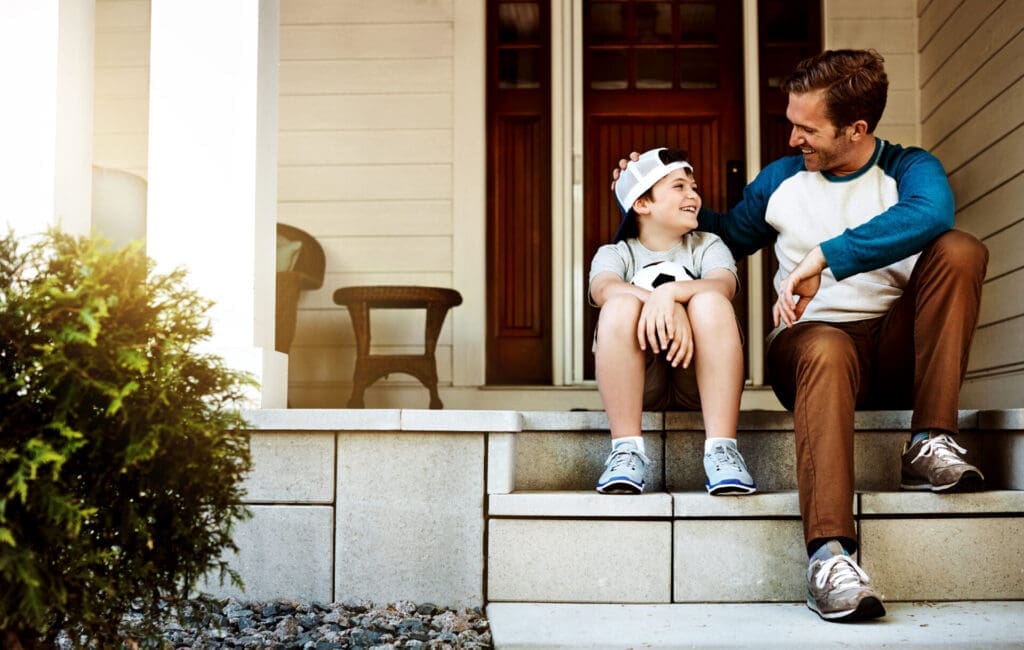 young boy and father sitting on a porch, talking and smiling