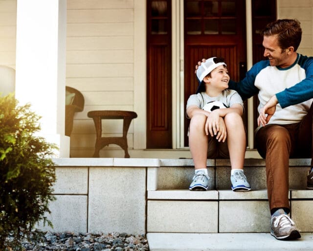 young boy and father sitting on a porch, talking and smiling