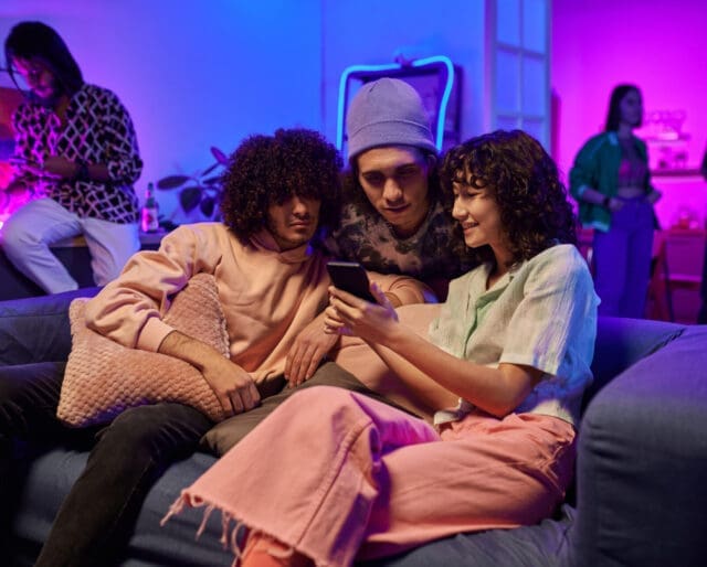 teens sitting on a couch at a party, looking at a phone