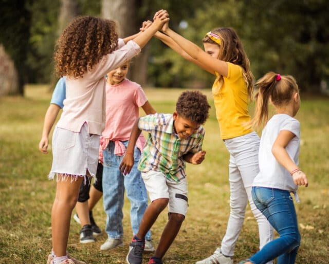 children playing outside, a boy running under the linked arms of two girls