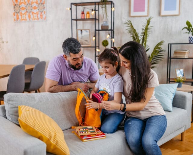 Young mother and father preparing their daughter for school. Packing a backpack together.