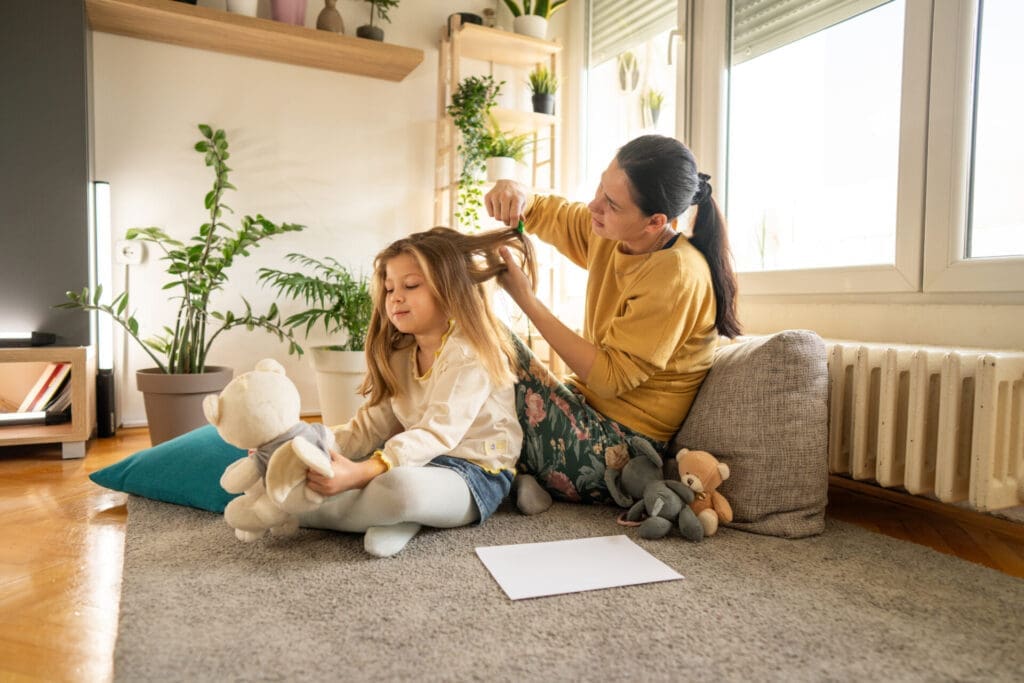 Getty images. Full length shot of mother doing head lice cleaning on little daughter while sitting on floor at home
