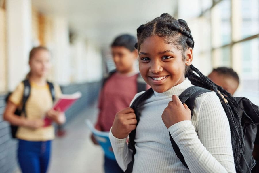 Portrait of a confident young girl standing in the hallway of school with her peers in the background