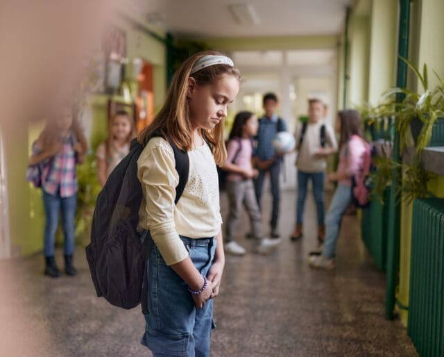 Elementary schoolgirl feeling depressed while standing out from the crowd in a hallway.