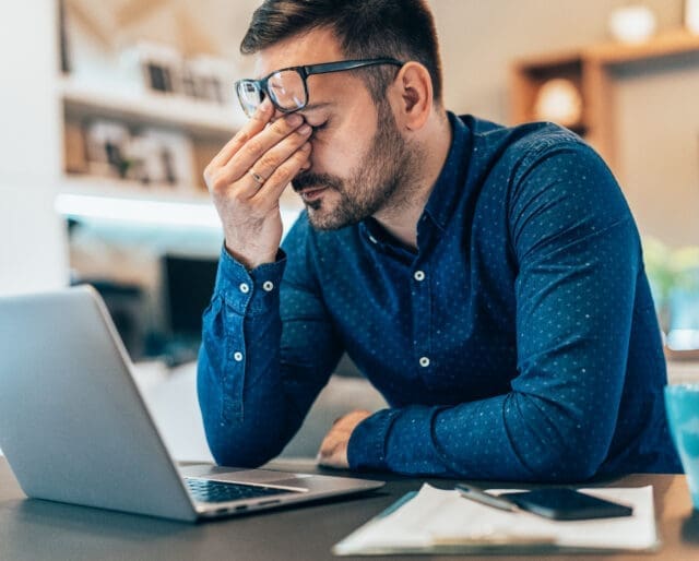 Tired young businessman working at home using lap top and looking Anxious