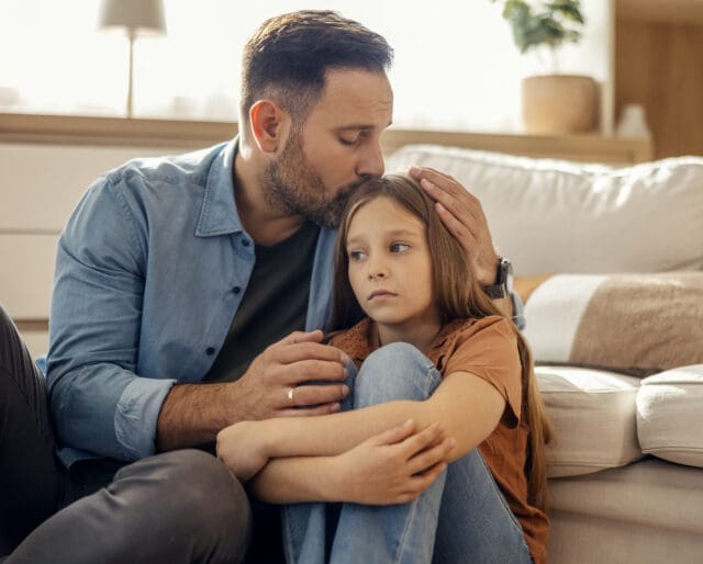 Loving father showing empathy, kissing his upset daughter's forehead, providing comfort and emotional support
